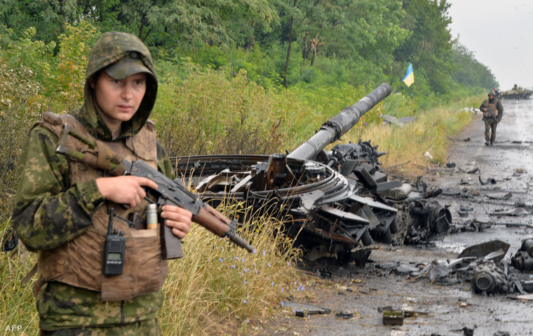 Egy ukrán fegyveres őrzi az oroszbarát szeparatisták kilőtt tankját az út mellett, Szlavjanszk közelében, 2014. július 7-én.