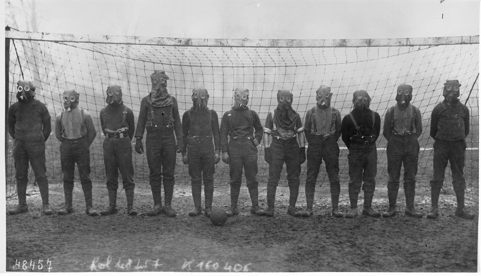 
                        1916, Franciaország északi része. Egy brit katonákból álló rögtönzött focicsapat pózol a hadszintéren hevenyészve összerakott futballkapu előtt. Azt, hogy kivel játszották a kép elkészülte utáni meccset, és tényleg gázálarcban voltak-e, nem tudni, utóbbi erősen kétséges. A sportélet az I. világháború alatt és közvetlenül utána sem állt meg - a fegyverek a labdarúgást nem tudták legyőzni. 
                        