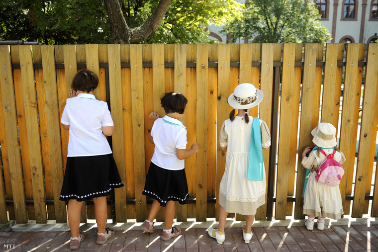Gyerekek néznek ki a kerítésen a Szent Anna Katolikus Óvoda új épületének udvarán