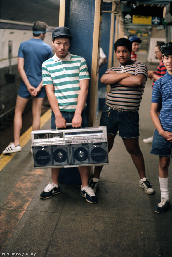 1983: fiatalok a metróban hatalmas boomboxszal, avagy ghettoblasterrel. A nagy teljesítményű hangfalakkal ellátott, hordozható kazettás magnók egy egész generáció kultikus jelképei lettek a nyolcvanas években, főleg a nagyvárosokban, a fekete és latino fiatalok között. New Yorkban a város egyik ikonikus zenekara, a Beastie Boys csinált divatot belőle.
                        