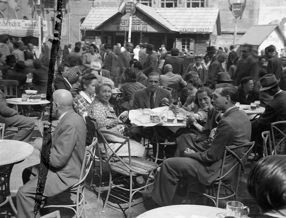 Az 1949-es Budapesti Őszi Vásár polgárinak tetsző látogatói sörrel és zsírpapírba csomagolt elemózsiával. Egy oszlopon még a Kossuth-címer látható, de azt néhány héten belül országszerte leváltotta a Rákosi-féle búzakoszorús, kalapácsos változat.