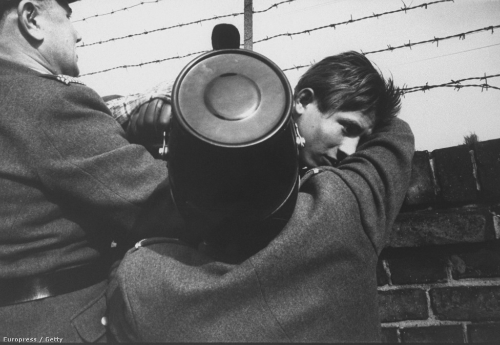 Két nyugatnémet rendőr segít át egy 17 éves fiút 
                        a falon. A becslések szerint a fal fennállásának 29 éve alatt körülbelül tízezren próbáltak meg átszökni Nyugat-Berlinbe, és 5000-en járhattak sikerrel.