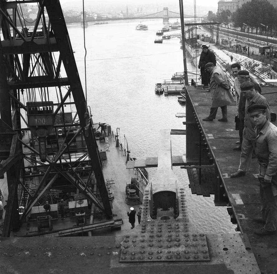 Az Erzsébet híd építése, az utolsó előtti pályaegység beemelése a pesti hídfőnél, háttérben a Lánchíd, 1964. A 100 tonna súlyú, 10 m hosszú, 20 m széles hídszakaszokat az Összekötő vasúti híd előtt elhelyezkedő szerelőtelepen állították össze, majd úsztatták az épülő hídhoz.