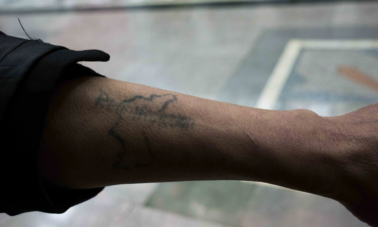 Az egységes Korea körvonalát ábrázoló tetoválást mutatja turistáknak egy leszerelt katona Phenjanban